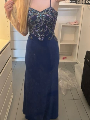 Balklänning  - Elegant blå långklänning med smala axelband och vackra paljettdetaljer över bysten och ryggen. Klänningen har figurnära passform upptill och faller rakt ner. Perfekt för bal, bröllop eller festliga tillfällen. Använd en gång på bröllop. Pris kan diskuteras.