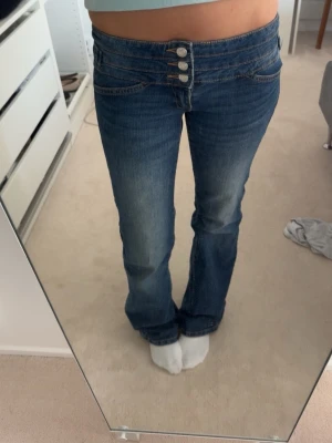 Blå bootcut jeans  - Snygga blå bootcut jeans med tre knappar framtill. Jeansen har inga fickor där back! Skriv för frågor och prisförslag, midjemått tvärs över är 37cm, innerbenslängd är 82cm