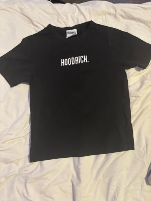  Hoodrich t shirt - Svart t-shirt från Hoodrich med vit logga tryckt på bröstet. Klassisk passform med rund hals och korta ärmar. Perfekt för en streetwear-look och enkel att matcha med andra plagg.