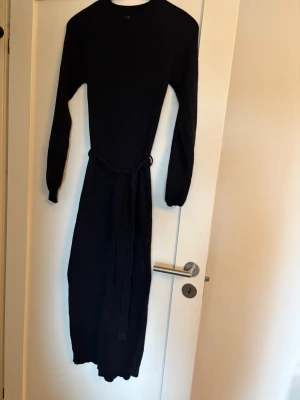 Svart stickad klänning Bubbleroom - Lång tight svart stickad klänning från Bubbleroom med rund halsringning och långa ärmar och slitz bak. Klänningen har ribbstickat material och ett knytskärp i midjan. Använd en gång men för tight för min smak. 
