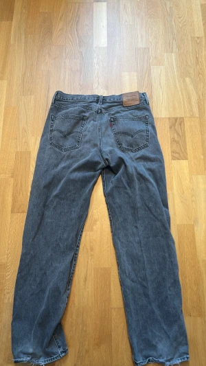 Levi's Stay Loose gråa jeans - Säljer ett par gråa Levi's Stay Loose jeans med raka ben och klassiska bakfickor. Jeansen har en avslappnad passform och är tillverkade i denim med tydliga sömmar och läderpatch bak i midjan. Perfekta för en chill och trendig look.