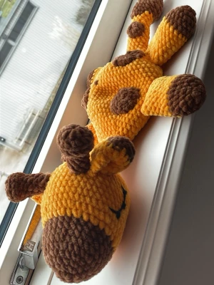 Virkad giraff i gult och brunt - Söt handvirkad giraff i mjukt garn med gula och bruna detaljer. Giraffen har bruna fläckar, öron och horn samt broderade ögon. Ingen stoppning i kropp och ben vilket gör den perfekt som sovkompis/snutte till ett litet charmtroll.