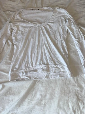 Vit långärmad topp med spetskant - Osäker på storleken då lappen är bortklippt! Söt vit långärmad topp med v-ringning och fin spetsdetalj runt halsen. Tunn och mjuk i materialet. Tyvärr lite sliten i spetsen och ett hål o ryggen!