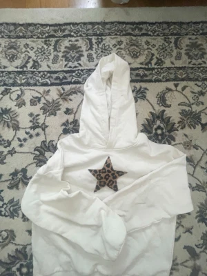 Vit hoodie med leopardstjärna🐆 - Säljer en vit hoodie med en stor stjärna i leopardmönster på bröstet. Hoodien har klassisk huva och är tillverkad i mjukt tyg, perfekt för en avslappnad och trendig look. Inga synliga loggor eller märken. Har aldrig använt den.🐆🤍🫶🏽