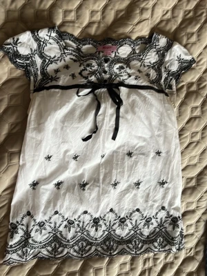Gullig blus med rosett - Vit blus med broderi gs mönster och svart rosett. Har dragkedja på sidan. Och tyvärr gula fläckar från en tidigare användare. Se bilder