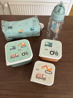 Turkos matlådeset med fordon - Säljer ett set med tre matlådor, en vattenflaska och ett pennfodral från Turtle. Alla delar är turkosa med söta tryck av olika fordon som grävmaskiner, traktorer och lastbilar. Matlådorna är fyrkantiga i olika storlekar och pennfodralet har dragkedja med fordonshänge.