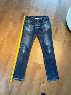 Nudie Jeans Grim tim - Säljer mina nudie jeans, modell grim tim med naturlig slitage från telefon och plånbok.  Mått:   	•	Midja: ca 38 cm 	•	Innerben: ca 79–80 cm 	•	Ytterben: ca 104–105 cm 	•	Lårbredd: ca 22–23 cm  Måtten är ungefärliga (±1 cm)  Bara att hojta vid eventuella frågor!