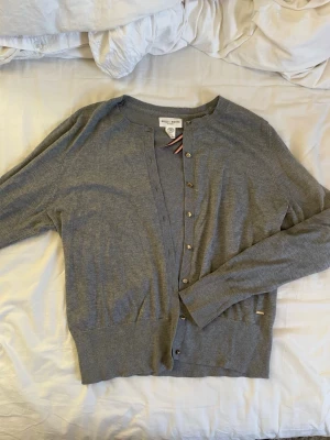 Grå kofta från Holly & Whyte - Mörkare grå kofta från Holly&Whyte med små knappar i guld. Mjukt och inte alls stickigt material. Den är i L men är mindre i storlek. 