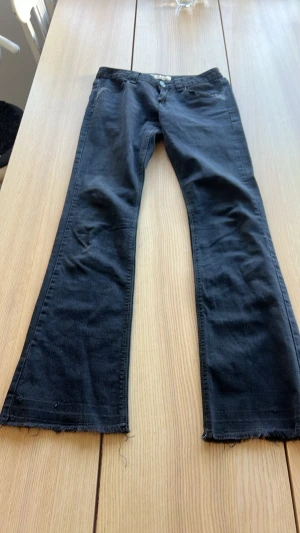Svarta bootcut jeans med rå kant - Säljer ett par svarta bootcut jeans med trendig rå kant nertill. Jeansen har klassisk femficksmodell och är tillverkade i mjukt denimtyg. Perfekta för dig som gillar en avslappnad och edgy stil.