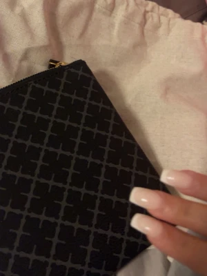 Svart axelväska med grafiskt mönster - Snygg svart axelväska med grafiskt rutmönster i grått. Väskan har justerbar axelrem och guldfärgade detaljer. Tillverkad i ett tåligt konstlädermaterial och stängs med dragkedja. Perfekt för dig som gillar stilrena accessoarer med en twist.OPS det är ej lapp kvar på väskan