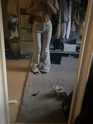 Ljusgråa bootcut jeans - Säljer ett par ljusgråa bootcut jeans med klassisk femficksmodell och låg midja. Jeansen har vida ben och är tillverkade i ett mjukt denimtyg som ger en avslappnad look. Perfekta för dig som gillar retrostil och vill ha ett par riktigt snygga jeans.