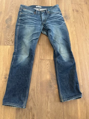  Acne Jeans - Snygga blå jeans från Acne Jeans med raka ben och klassisk femficksmodell. Jeansen har en tvättad look med ljusare partier och detaljer i kopparfärgad metall. Perfekta för en avslappnad och trendig stil.