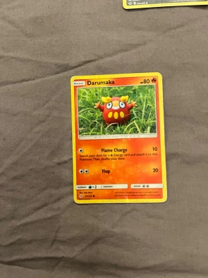 Pokémonkort Darumaka - Säljer ett Pokémonkort med Darumaka-motiv. Kortet har en färgstark design med röd och gul färg, och är tillverkat i klassiskt pappmaterial. Perfekt för samlare eller dig som gillar Pokémonspel.