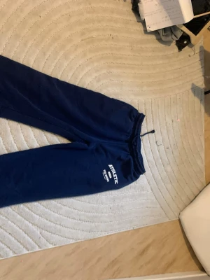 Mörkblå mjukisbyxor från RS SISTER - Mörkblå mjukisbyxor från RS SISTER med trycket 'ATHLETIC' på ena benet. Byxorna har resår och dragsko i midjan samt mjukt fleecematerial på insidan. Perfekta för chill eller träning. Passar som Xs S M L