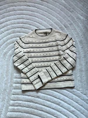 Beige stickad tröja med svarta ränder - Snygg beige stickad tröja från LDY med svarta horisontella ränder och små prickar i mönstret. Tröjan har rund halsringning, långa ärmar och ribbade muddar. Perfekt för dig som gillar en stilren och mysig look.