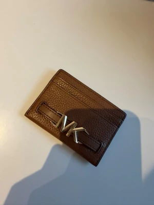 Brunt korthållare från Michael Kors - Snygg brun korthållare i äkta läder från Michael Kors med guldfärgad MK-logga framtill. 