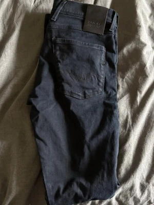 Svarta jeans från Replay Anbass - Säljer ett par svarta slim fit jeans från Replay, modell Anbass. Jeansen har klassisk femficksdesign, svarta sömmar och läderpatch med logga bak i midjan. Materialet är mjukt och stretchigt för extra komfort. Lengdeb är storlek 34 och midjan är 31.