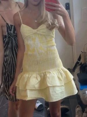 Gul kortklänning med volanger - Söt gul kort klänning med tunna axelband och volang nertill. Klänningen har ett diskret rutigt mönster och en v-ringad överdel. Perfekt för sommaren!❣️byter helst mot en likadan i storlek S!!! TRYCK INTE ”KÖP NU”! BUDA!!