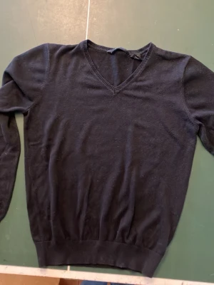 Svart V-ringad stickad tröja Abacus - Svart stickad tröja från Abacus i storlek XS. Tröjan har en klassisk V-ringning och långa ärmar. Perfekt basplagg i garderoben och lätt att matcha med olika stilar. Tillverkad i mjukt material för en bekväm känsla.