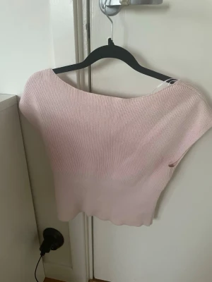 Ljusrosa ribbad ärmlös topp - Supersöt ljusrosa ribbad topp med v-ringning och ärmlös design. Toppen har en mjuk, stickad känsla och en lätt croppad passform. Perfekt att styla med jeans eller kjol för en fräsch look.