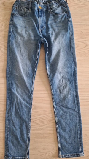 Ljusblå ungdomsjeans från HM, super stretch,  stl 164 - Snygga ljusblå jeans med klassisk femficksdesign och gylf med knapp från HM,Super Stretch. Jeansen har en slim fit-modell och är tillverkade i stretchigt denimtyg för extra komfort. Perfekta för en avslappnad och trendig look.