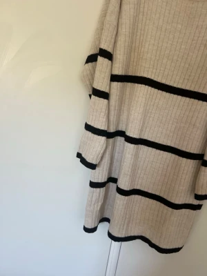 Beige stickad tröja med svarta ränder - Säljer en beige stickad tröja från Vigonez med svarta horisontella ränder. Tröjan har ribbstickad struktur, rund halsringning och långa ärmar. Perfekt för dig som gillar en enkel men snygg stil.