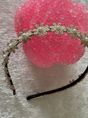 Guldig diadem med pärldetaljer - Superfint diadem med blommiga detaljer och små vita pärlor. Perfekt accessoar för att lyfta din frisyr med en elegant touch. Blommorna är broderade och pärlorna sitter i mitten av varje blomma. Metallbas med mjuk insida för bekväm användning. Finns fler kvar, helt ny 