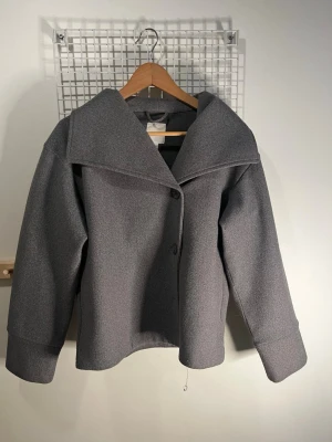 Grå ulljacka med bred krage - Stilren grå jacka med bred krage och knäppning framtill. Jackan har en rak, något boxig passform och är tillverkad i ullmaterial.💕💕