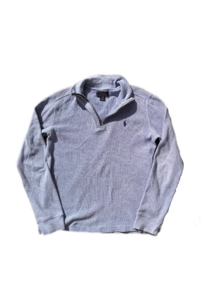 Ljusblå tröja från Polo Ralph Lauren - Ljusblå långärmad tröja från Polo Ralph Lauren med halv dragkedja och klassisk krage. Tröjan har diskret broderad logga på bröstet och är tillverkad i ett mjukt, strukturerat material. Perfekt för en avslappnad och stilren look.