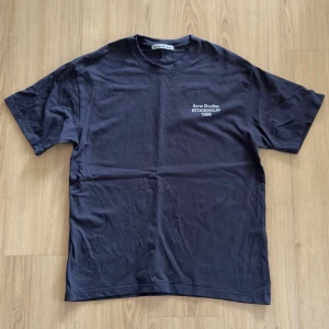 Mörkblå t-shirt från Acne Studios - Snygg mörkblå t-shirt från Acne Studios med tryck 'Acne Studios Stockholm 1996' på bröstet. Klassisk passform med rund hals och korta ärmar. Perfekt för en clean och stilren look.