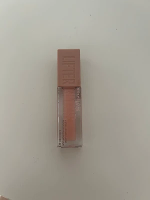 Maybelline Lifter Gloss 002 Ice - Maybelline Lifter Gloss i nyansen 002 Ice. Ett läppglans med transparent, ljusrosa ton och glansig finish. Kommer i en stilren fyrkantig plastförpackning med bred applikator och rosabeige lock. Perfekt för att ge läpparna en fylligare look.