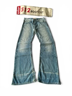 Levi's 512 Bootcut ljusblå jeans - Ljusblå bootcut jeans från Levi's, modell 512. Jeansen har en klassisk femficksdesign, slitna detaljer och breda ben. Tillverkade i denim med vintagekänsla och tydliga tvättade partier. Perfekta för dig som gillar retrostil och avslappnad look.