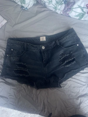 Svarta slitna jeansshorts från Zuki - Säljer ett par svarta lågmidjade jeansshorts från Zuki. Står att strl är 44 men skulle säga att den mer är 38. 