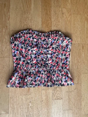 Blommig korsett topp från h&m - Supersöt korsett topp med blommigt mönster i rosa, lila och blå toner. Toppen har volang nertill och rynkade detaljer framtill. Superfin och perfekt till sommaren. Köpt secondhand men har aldrig använts pga att den är för liten. Storlek 38 men är rätt så liten i storleken. Kan gärna byta mot en likadan topp i storlek 40!💞