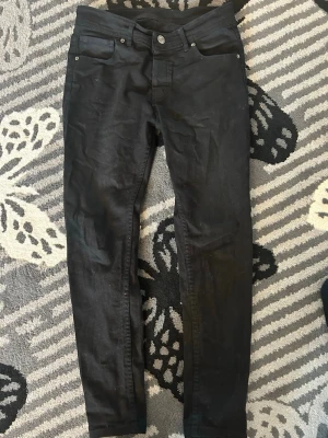 Svarta skinny jeans - Säljer ett par svarta skinny jeans med klassisk femficksdesign och smal passform. Jeansen har normalhög midja och stängs med knapp och dragkedja. Perfekta till en avslappnad streetstyle-look.