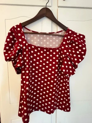 Röd prickig blus med puffärmar - Trendig röd blus med vita prickar och stora puffärmar. Fyrkantig ringning och figurnära passform. Perfekt för dig som vill sticka ut med en färgglad och lekfull topp.