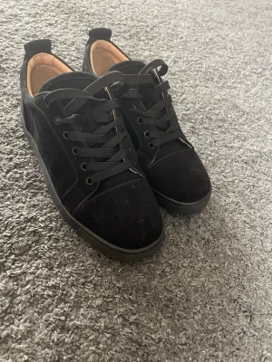 Svarta sneakers från Christian Louboutin - Snygga svarta sneakers i mocka från Christian Louboutin med klassisk röd sula och svarta skosnören. Låg modell med diskret logga på sulan och mjukt beige foder. Perfekta för dig som gillar stilrena och exklusiva skor. Pris kan diskuteras  använda i ca 1-2 veckor säljer för de e för små