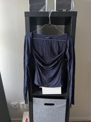Mörkblå långärmad topp Gina Tricot - Snygg mörkblå långärmad topp från Gina Tricot med draperad front och bred urringning. Tillverkad i mjuk bomullsmix som sitter skönt mot kroppen. Perfekt för dig som gillar en enkel men trendig stil.