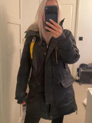 Svart jacka från Parajumpers - Säljer en svart jacka från Parajumpers i storlek XS med gul detalj vid kragen och patch på ärmen. Jackan har huva med fuskpäls och stora fickor. Finns ett hål i luvan men ska inte vara något problem att sy ihop. Nypris 9499kr