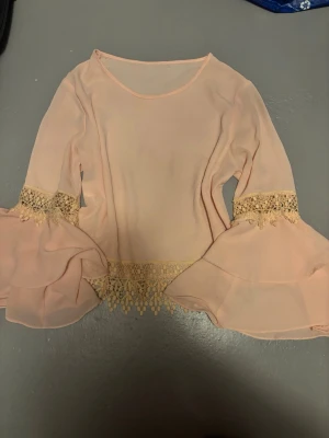 Ljusrosa blus med volangärmar köpt utomlands - Supersöt ljusrosa blus i transparent chiffong med vida volangärmar och spetsdetaljer vid ärmslut och midja. 