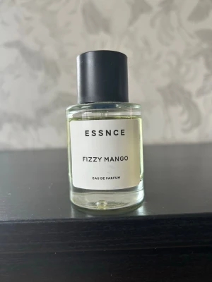 ESSNCE Fizzy Mango Eau de Parfum - Fräsch parfym från ESSNCE, doften Fizzy Mango. Flaskan är cylindrisk i genomskinligt glas med svart plastlock och enkel vit etikett. Perfekt för dig som gillar fruktiga och upplyftande dofter. Säljer då jag har för många parfymer.