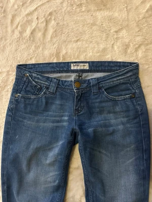 Blå lågmidjade bootcut jeans från Lee - Snygga blå jeans från Lee med låg midja och utsvängda ben. Storlek W26 L33 och passar mig som är 170cm lång och brukar ha XS/S. Perfekta för en avslappnad och trendig look.
