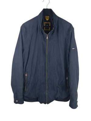 Pierre Cardin marineblå vårjacka, storlek 52 - En stilren jacka från Pierre Cardin i en mörkblå nyans. Jackan har en hel dragkedja framtill och två sidofickor med dragkedja. Ärmsluten är justerbara med knappar. Insidan av jackan har ett rutigt foder i vitt, rött, grönt och gult, samt en innerficka med dragkedja. En diskret Pierre Cardin-logotyp finns på vänster ärm. Armhåla till armhåla: 59cm Axelbredd: 47cm Långt: 74cm Armlängden från armhåla: 47cm