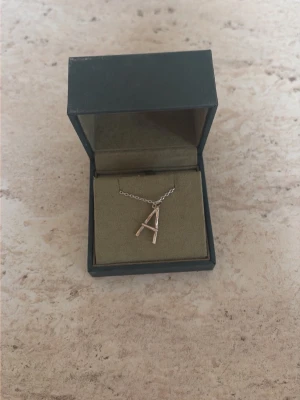 Silverhalsband med A-hänge Maria Nilsdotter - Snyggt halsband i silver från Maria Nilsdotter med ett stilrent A-format hänge. Kedjan är tunn och elegant, perfekt för dig som vill ha ett personligt smycke. Kommer i original ask. Nypris 1995 (2000kr) men säljer för 1250kr