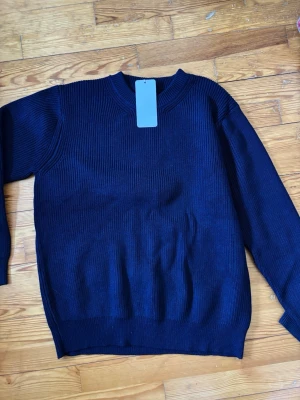 Mörkblå stickad tröja från Maison Margiela - Säljer en mörkblå stickad tröja från Maison Margiela. Tröjan har en klassisk rund halsringning och är ribbstickad med långa ärmar. Perfekt för dig som gillar stilrena och minimalistiska plagg. Materialet är mjukt och håller värmen.