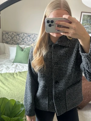 Kort rutig kappa  - Stilren svartvit kappa från Monki. Modellen har stora svarta knappar framtill, bred krage och raka ärmar. Perfekt till våren.