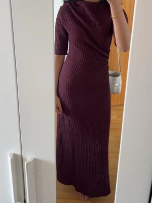 Vinröd långklänning med struktur - Säljer en vinröd långklänning med halvlånga ärmar och snygg struktur i tyget. Klänningen har en perfekt  passform och ett  slit längst ner vid höger ben. Köpt för 400kr