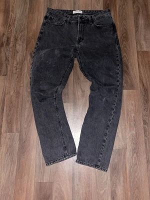 Svarta raka slim jeans - Säljer ett par svarta raka jeans med hög midja och klassisk femficksmodell. Jeansen har en tvättad look och raka ben, perfekta för en avslappnad stil. Materialet är kraftig denim i bomull. Passar dig som gillar en tidlös och enkel look.