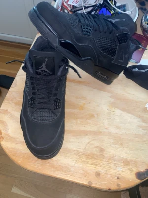 Jordan 4 black cat - Säljer ett par helsvarta Air Jordan 4 Retro sneakers med klassisk mesh och mockadetaljer. Skorna har högt skaft, ikonisk Jumpman-logga på plösen och robust sula. Perfekta för dig som gillar streetwear och vill ha en clean look.