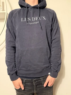 Mörkblå hoodie från Les Deux - Mörkblå hoodie från Les Deux med vit text 'LES DEUX copenhague' på bröstet. Klassisk känguruficka framtill, ribbade muddar och justerbar huva med snören. Tillverkad i mjuk bomullsblandning som känns skön mot huden. Perfekt för en avslappnad och stilren look. Pris kan diskuteras!💸 Strl: S✅ Hör av dig om du har funderingar!👍